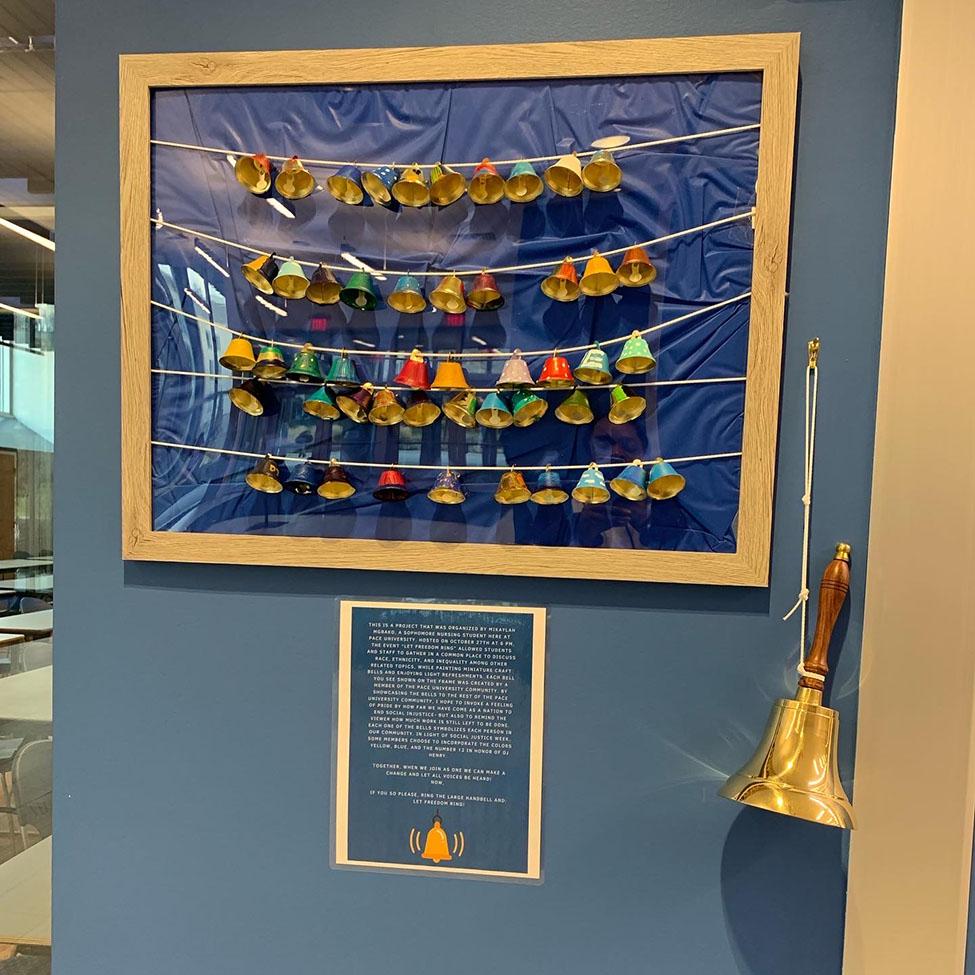 50 colorfully painted bells strung together on string, pinned to a blue background 