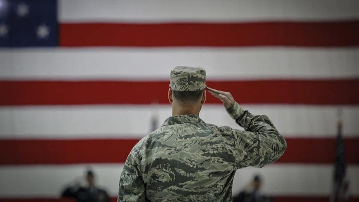 military airman in fatigues saluting the American flag