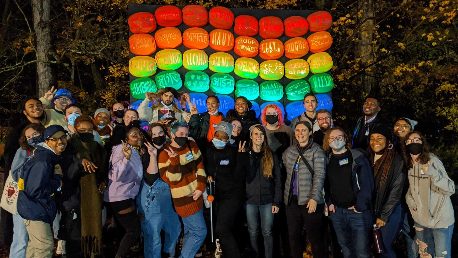 Students standing in front of a stack of pumpkins painted in rainbow colors