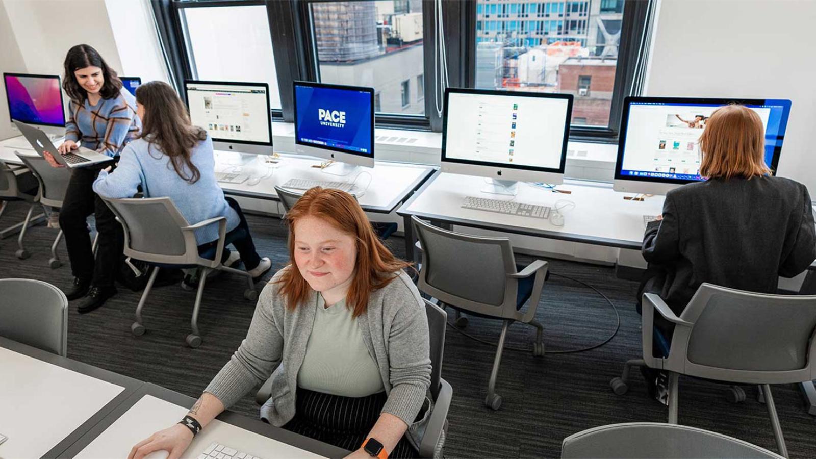 Students working in a computer lab. Outside the window is New York City.