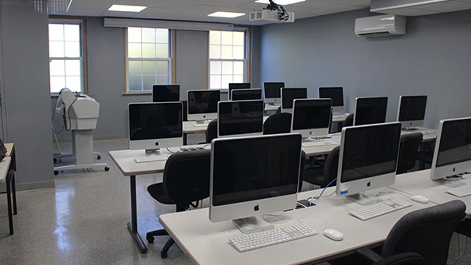Mac computers lined up on long tables in a well lit classroom