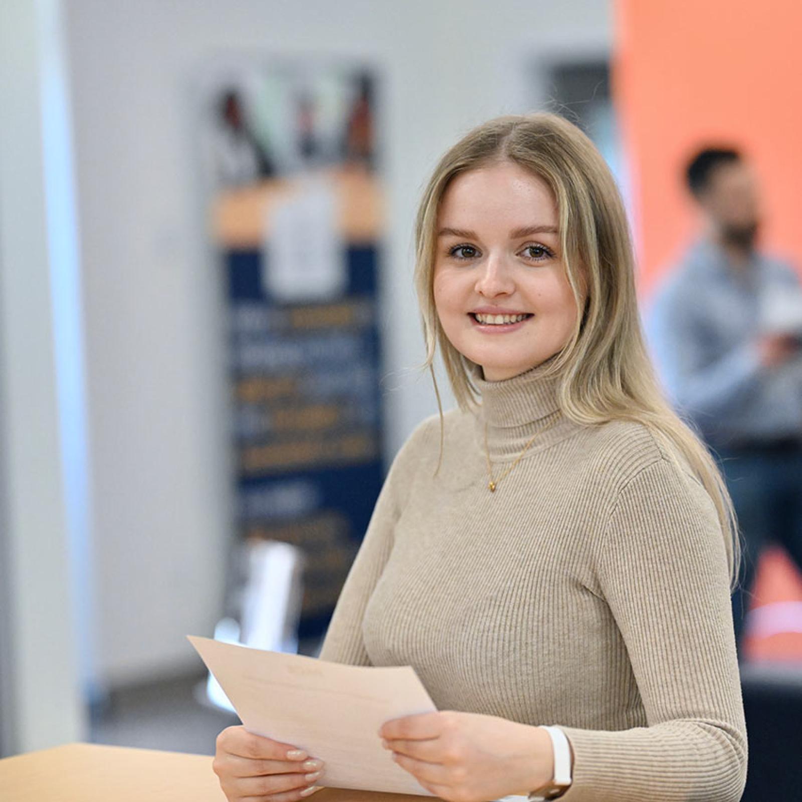 A Pace University student stands at a desk with some papers.