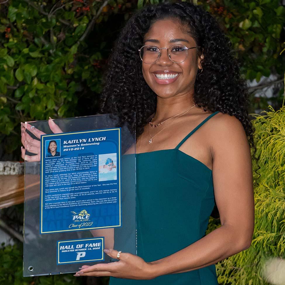 Kaitlyn Lynch, wearing a green dress, holds her Hall of fame plaque