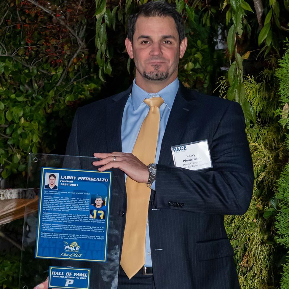 Larry Piediscalzo, wearing a dark suit and yellow tie, holds his Hall of Flame plaque