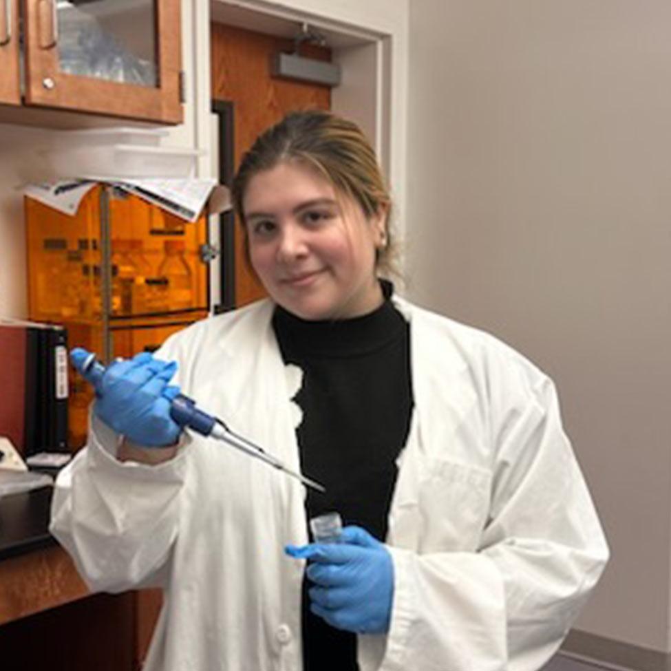 young woman at Pace University in a lab coat holding lab equipment