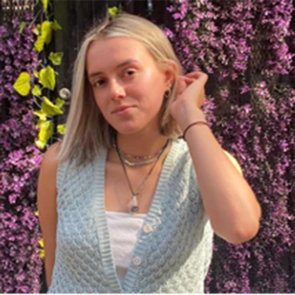 Portrait of Danielle Harari wearing a knitted sweater vest with flowers in the background