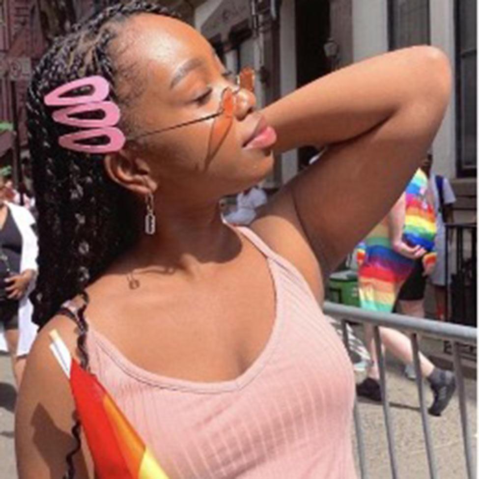 Portrait of Julie Bazile wearing a pink tank top with pink hair clips and orange tinted sunglasses