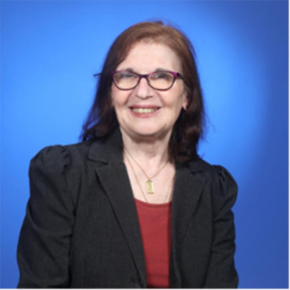 Portrait of Sharon Medow wearing a red shirt with a black jacket and a blue background