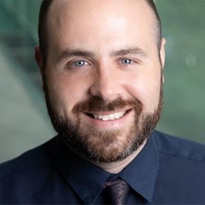 Portrait of Forrest Malloy wearing a dark blue dress shirt with a tie and a green background