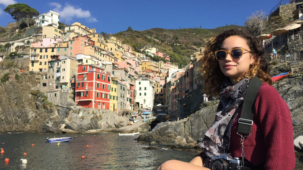 Lubin student Kaitlyn Jackson '19 sitting at the end of a harbor below a village on a hill during a semester abroad in England