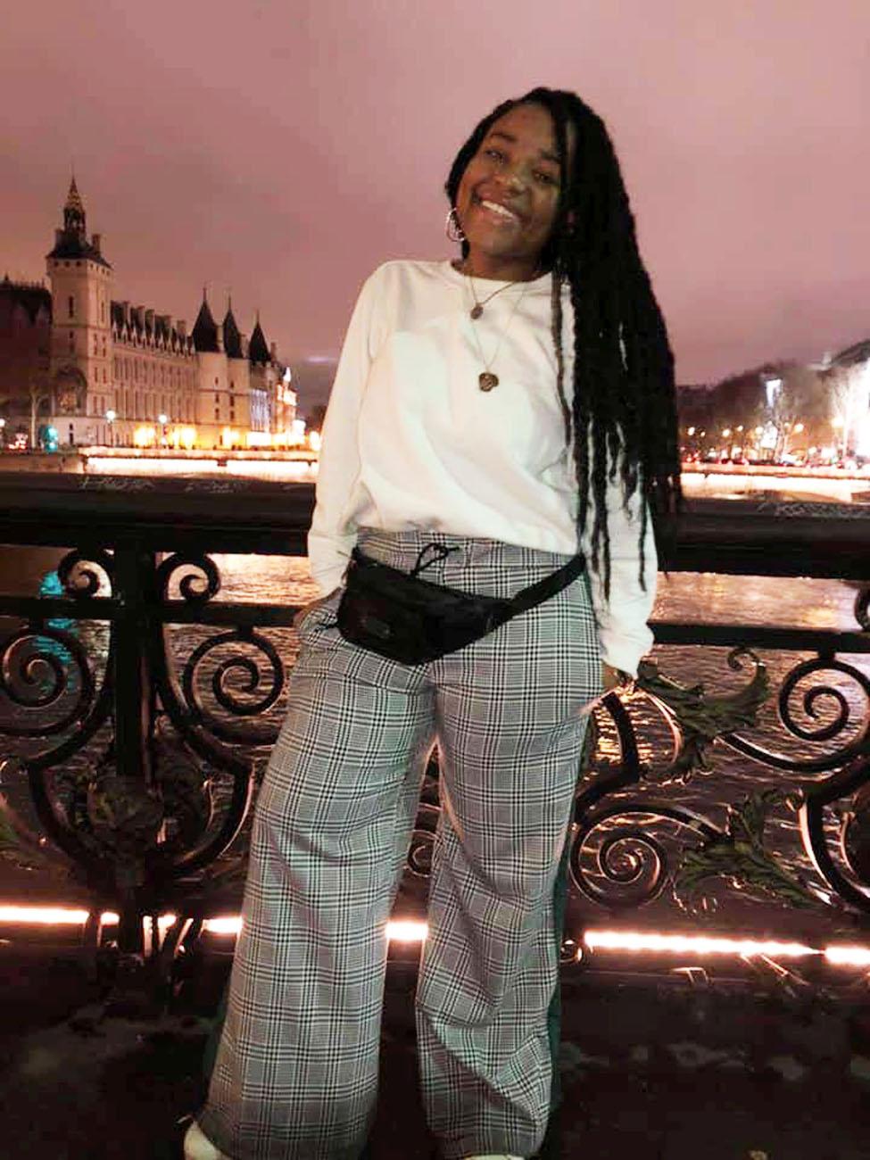 Lubin student Geanina Riley '21 standing next to cast-iron railing over a river in Paris with a chateau in the backgrond during her semester abroad in France