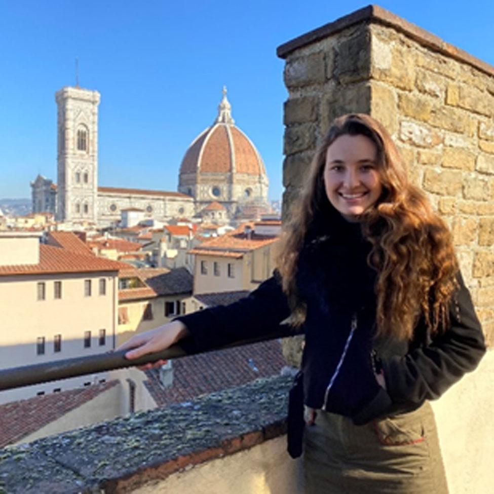 Lubin student Alexandra Godown '22 standing near a wall overlooking historic buildings in a city during her semester abroad in Italy