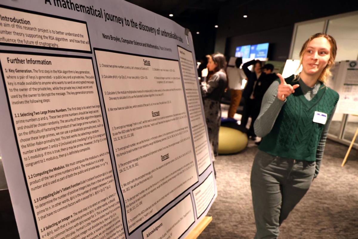 Female pointing to presentation board with information on mathematics research about a number theory's influence on cryptography.