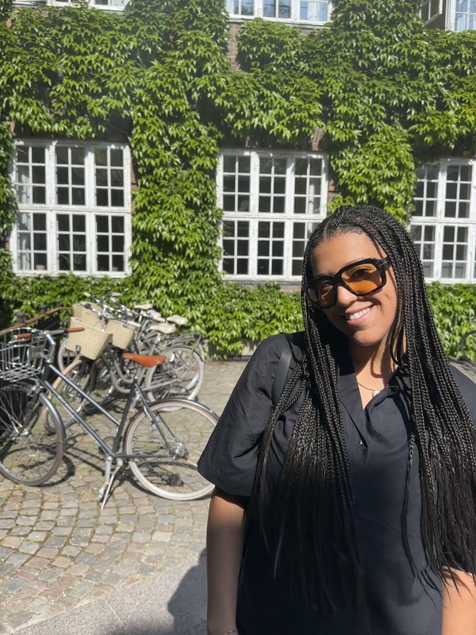 Pace University Lubin student standing in front of an ivy-covered building and bicycle rack during a 2023 field study to Denmark and Sweden