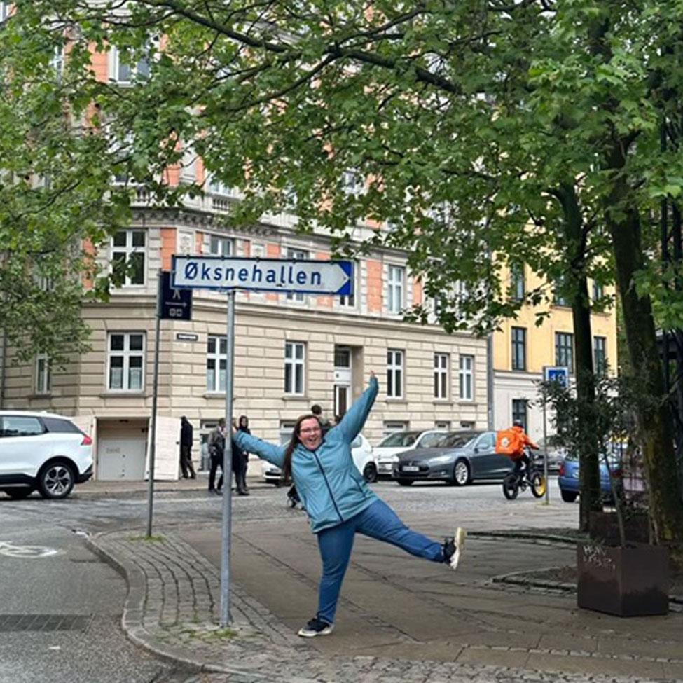Pace University Lubin student in front of a street sign in a leafy neighborhood of Copenhagen during a 2023 field study to Denmark and Sweden