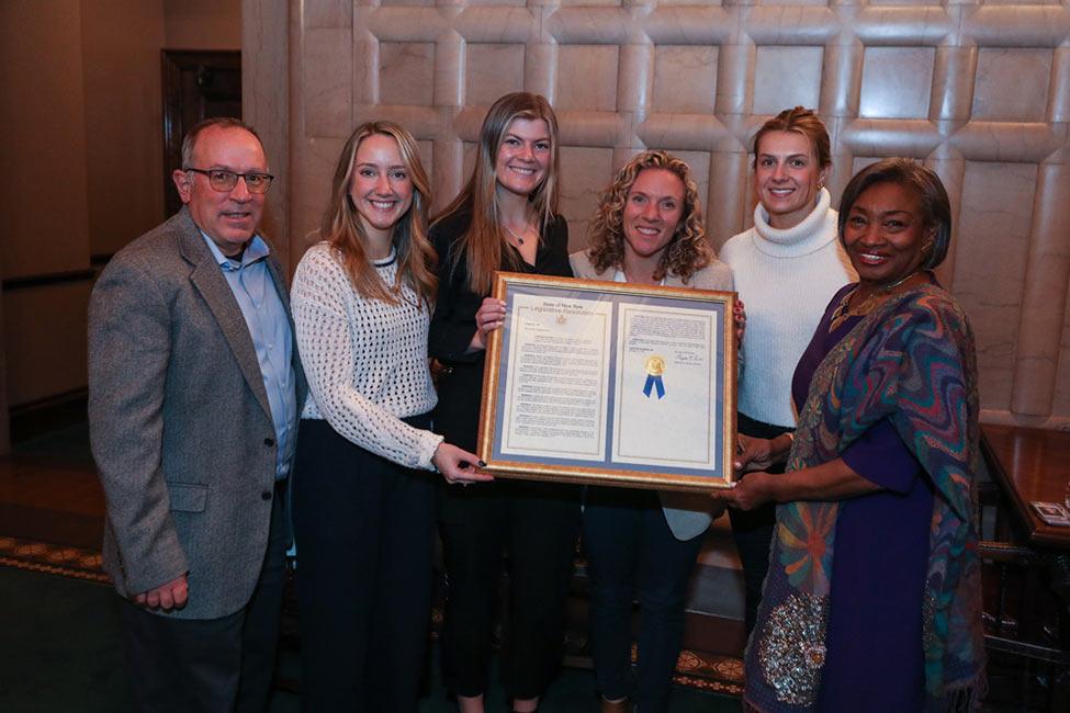 (From left) Volunteer Assistant Coach Robert Molfetta, Co-Captain Delilah Doyle, Co-Captain Kayla Conway, Head Coach Tricia Molfetta, Co-Captain Emma Rafferty, and Majority Leader Andrea Stewart-Cousins holding Senate Resolution No. 1667.