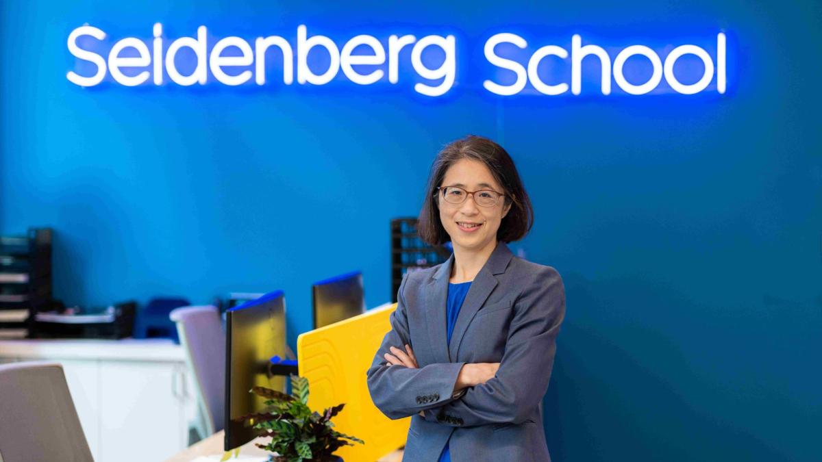 Pace Seidenberg's Interim Dean, Dr. Li-Chiou Chen, posing for a photo in front of a neon sign that says 'Seidenberg School'.