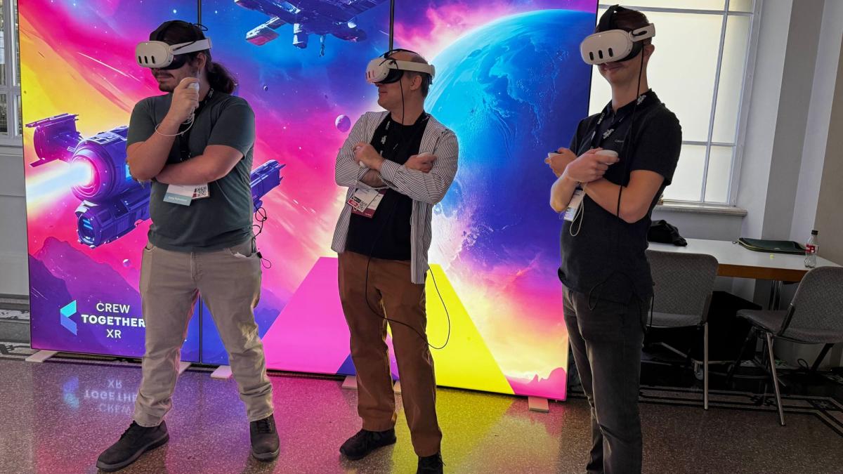 Pace Seidenberg professor Carmine Guida and two Seidenberg students standing in front of a colorful screen while trying out VR games.