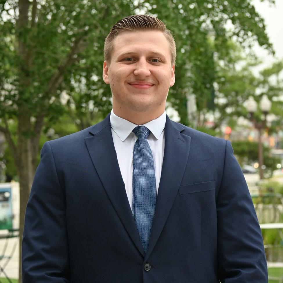 Pace student Adrian Brzozowski wearing a suit and posing for the camera.