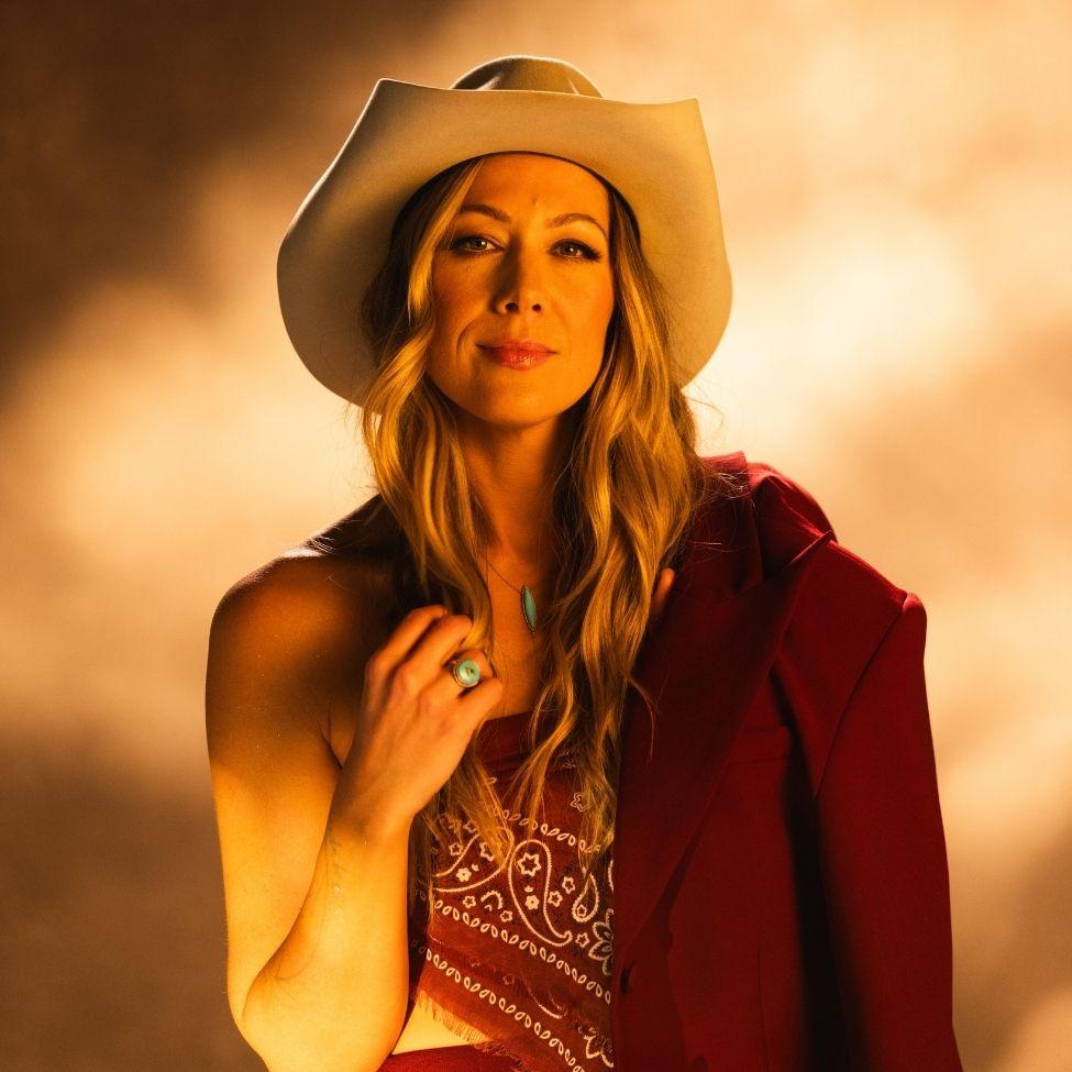 A headshot of singer Colbie Callait wearing a cowboy hat against a golden sunlit backdrop.