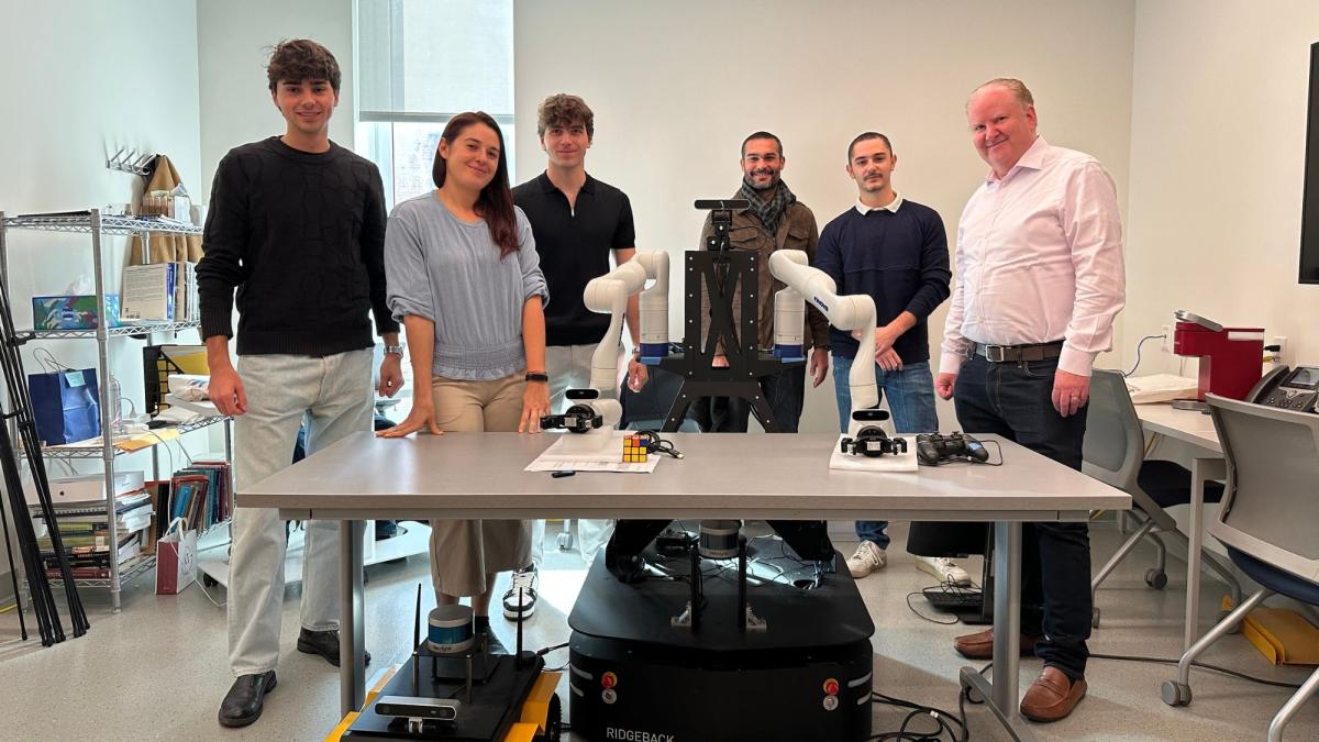 Sara Falcone posing for a photo in Seidenberg's Robotics Lab with colleagues from UCBM and Seidenberg professor Darren Hayes.