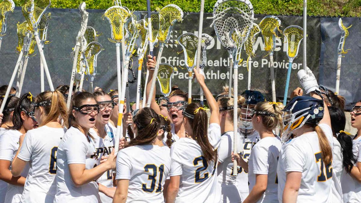 Pace women's lacrosse team holding their sticks in the air.