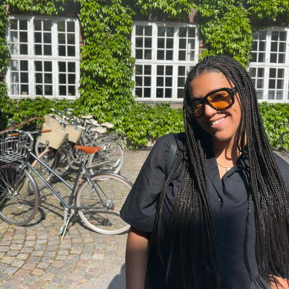 Pace University Lubin student standing in front of an ivy-covered building and bicycle rack during a 2023 field study to Denmark and Sweden