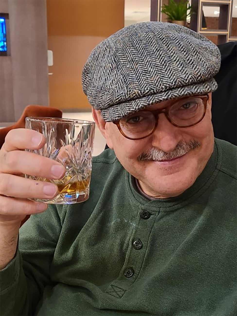 Steve Brodsky wearing a hat and toasting with a glass.