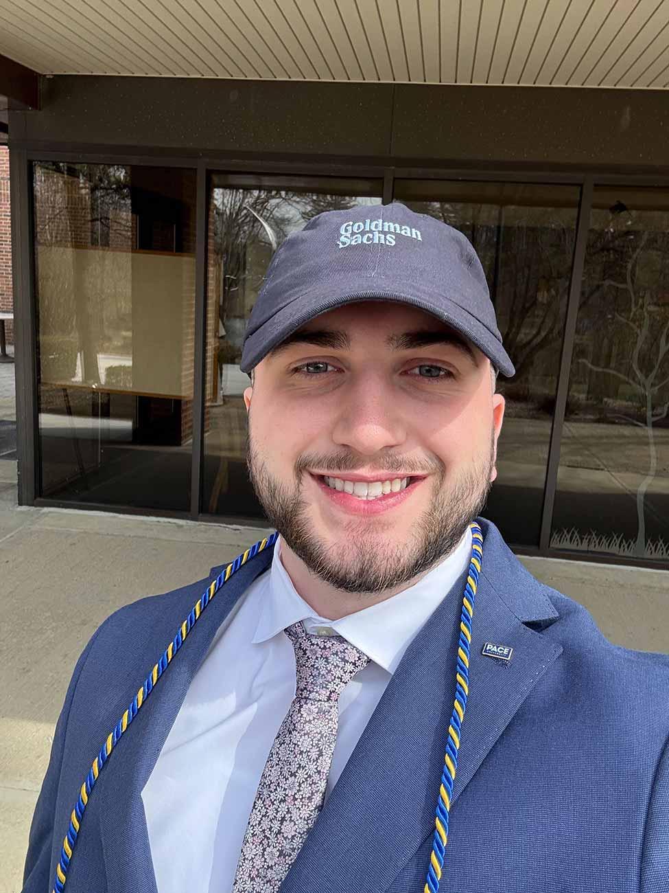 Evan Glusic wearing a suit and a Goldman Sachs baseball cap.