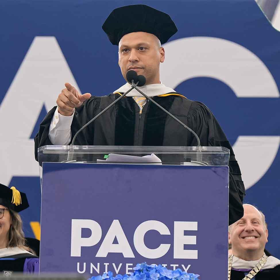 Pace alumni and news anchor Pedro Rivera wearing commencement regalia points at the crowd