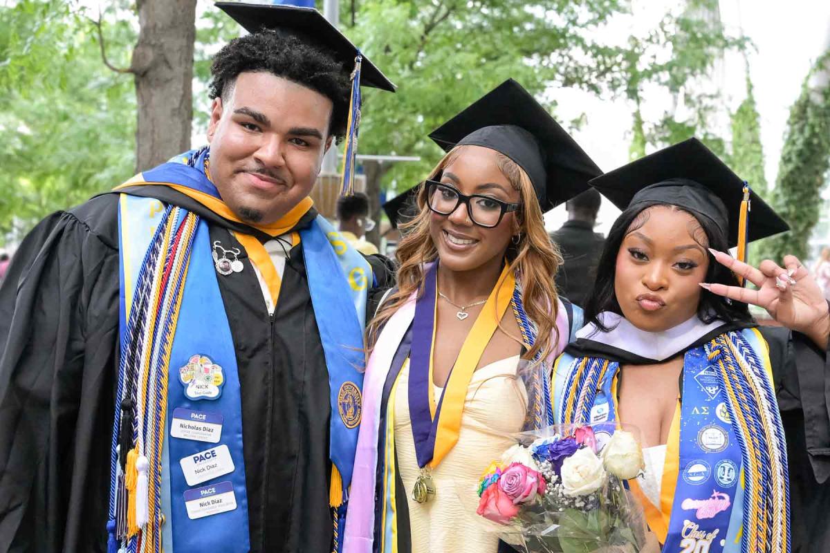 Three Pace graduates on Commencement day wearing their caps and gowns and posing for the camera.
