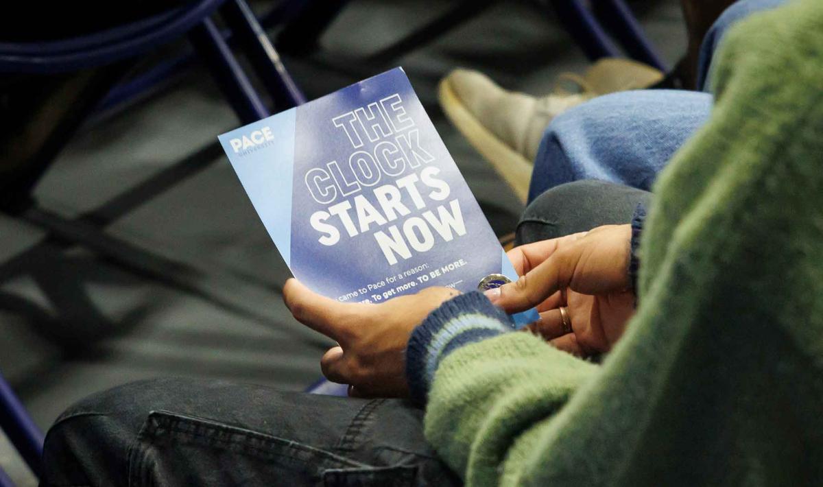 A student holds a flyer reading "The Clock Starts Now"