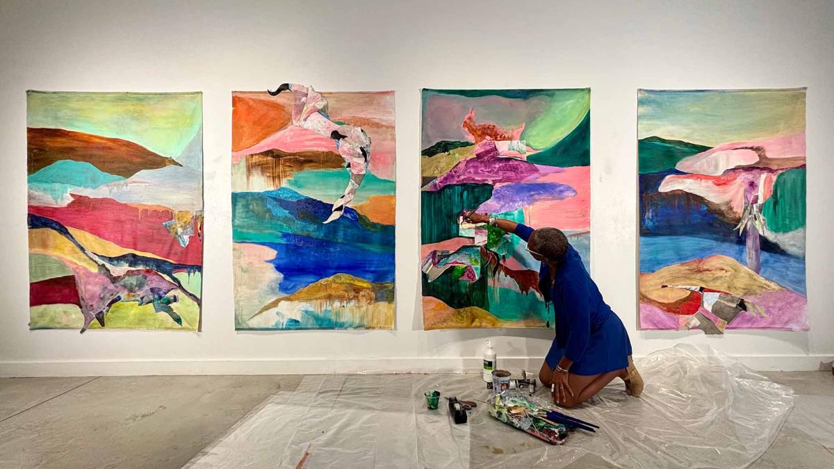 La Vaughn Belle kneels in front of a series of her paintings.
