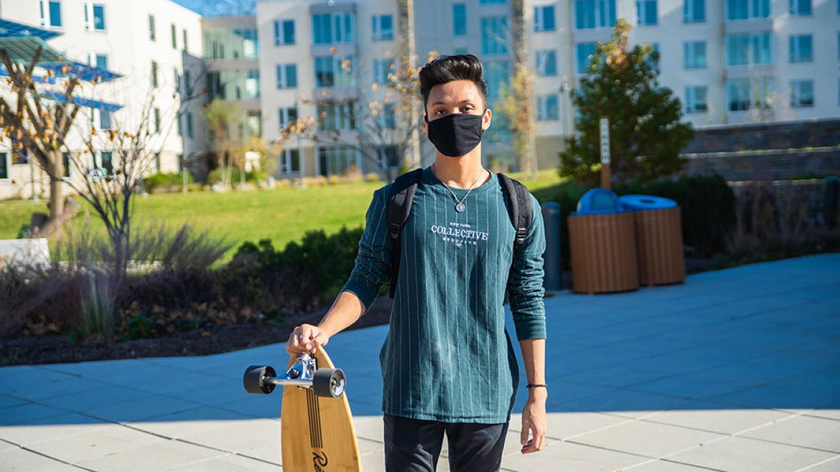 Student standing with his longboard on the Pleasantville campus