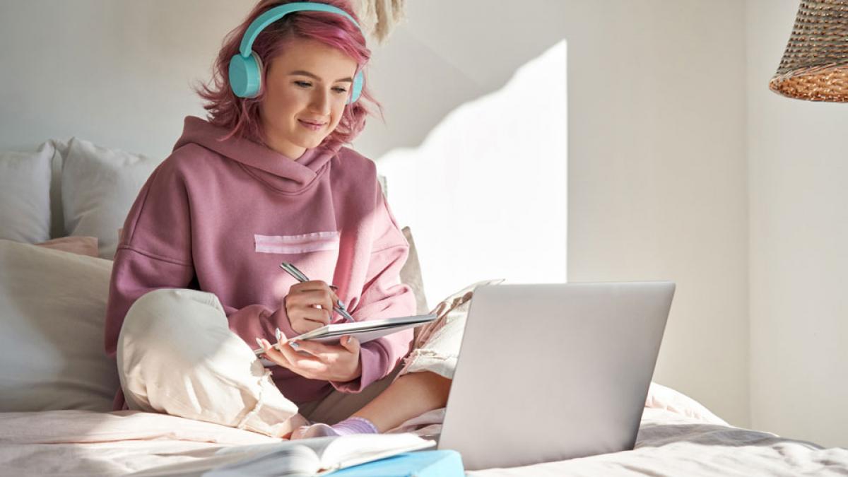 Student sitting on her bed taking online classes on her computer.