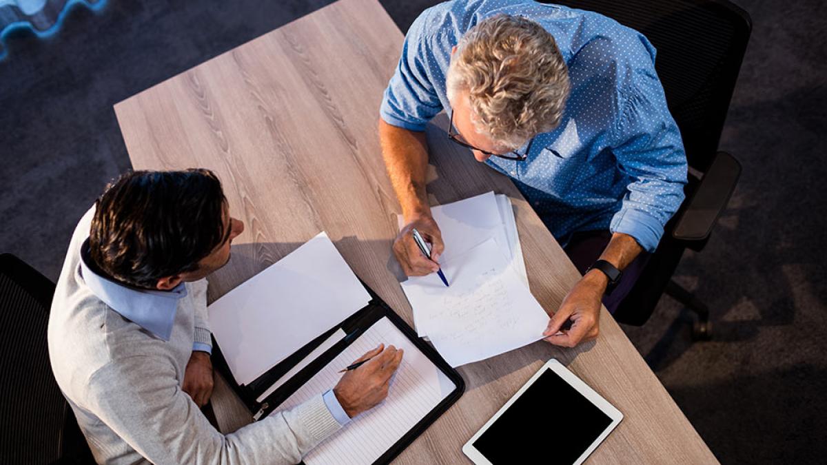 Two people sitting at a table, signing documents