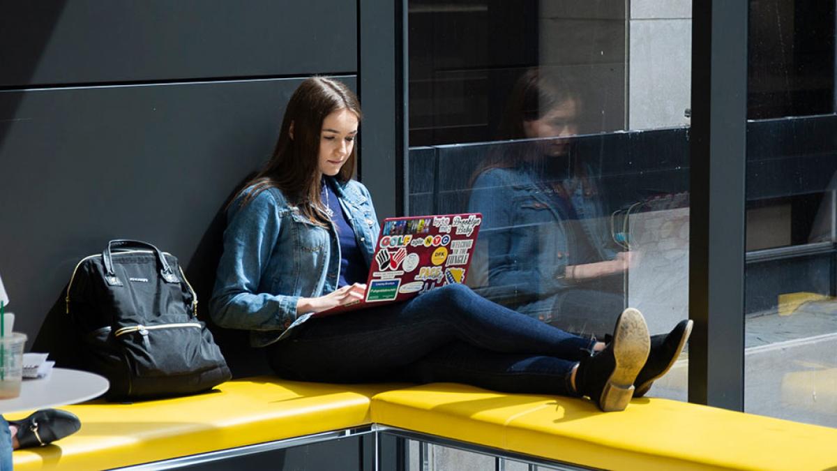 Student sitting on a bench working on her laptop.