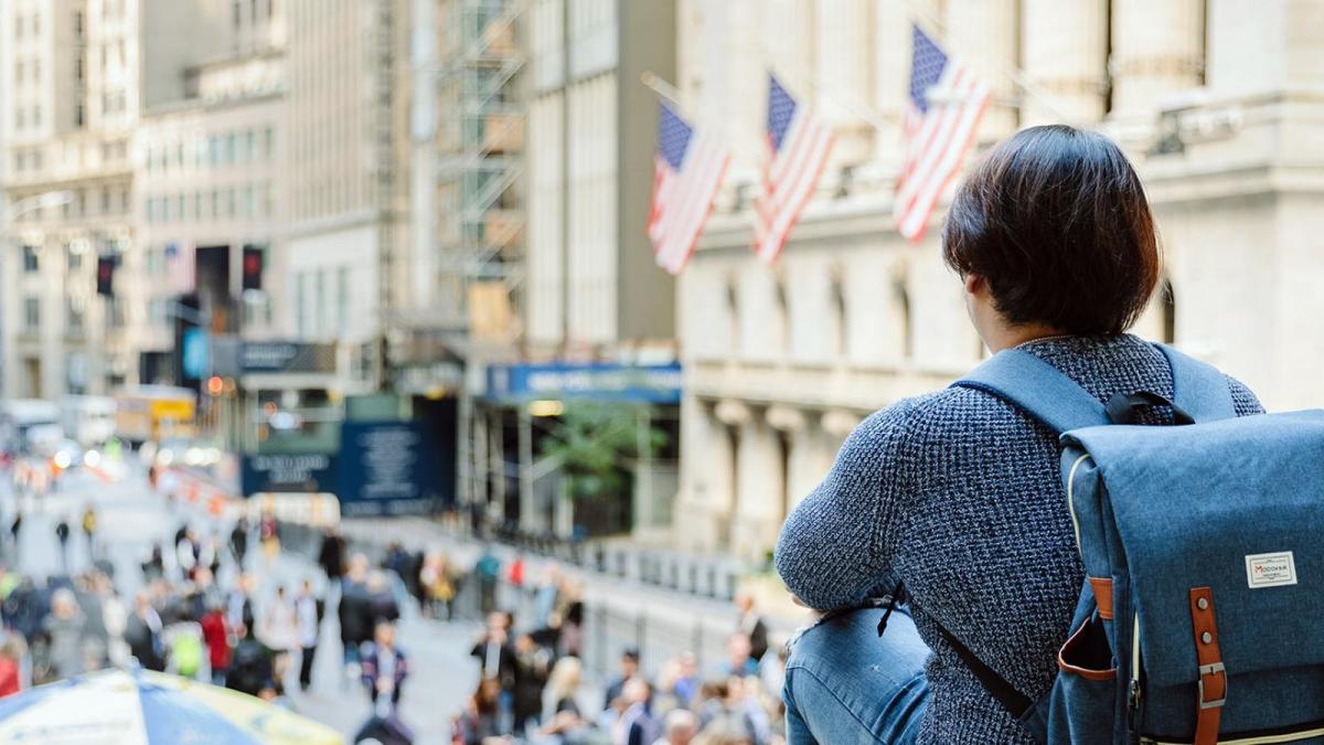 Student wearing a backpack looking at people walking around in NYC.