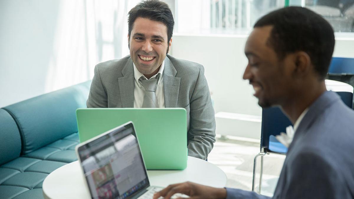 Two people sitting in front of their computers collaborating on a project.