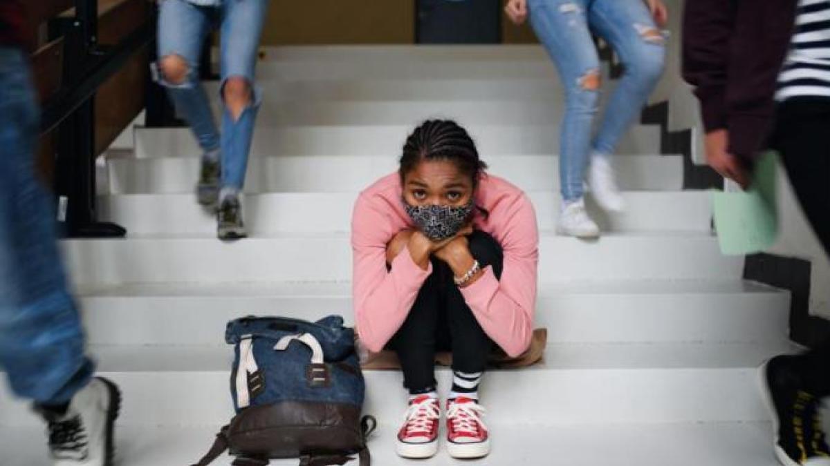 Student huddled sitting on steps surrounded by people walking.