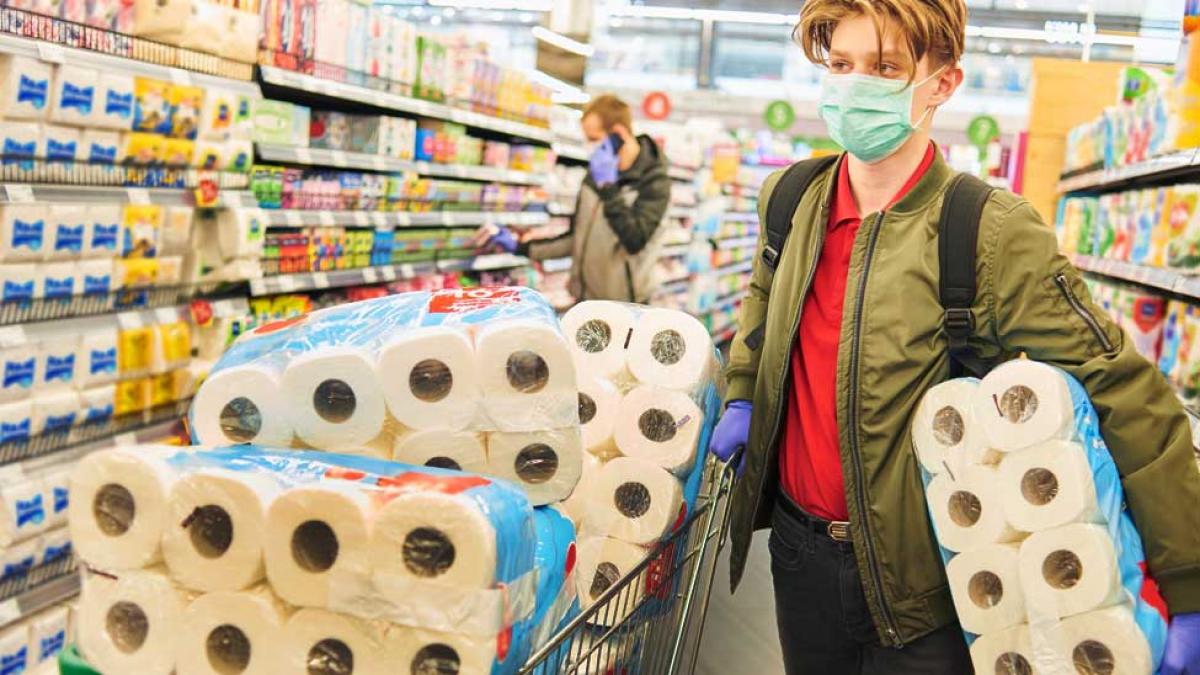 person in a grocery store with a cart full of toilet paper