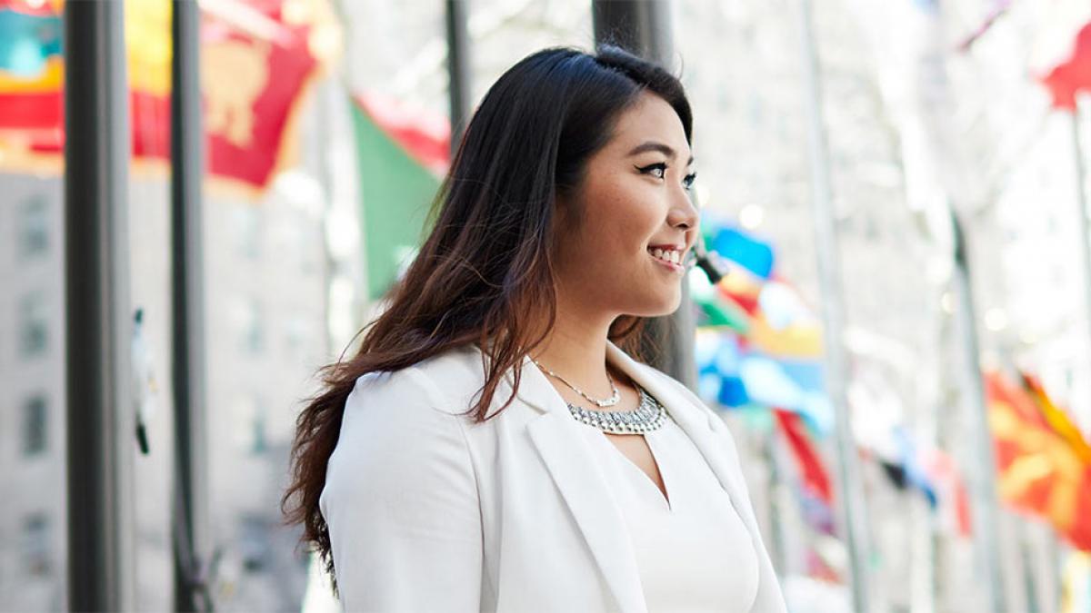 Female asian student in front of a row of international flagpoles
