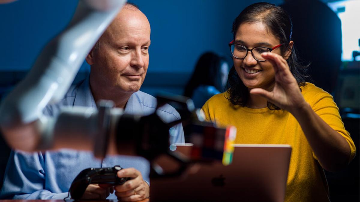 a faculty member and a student looking at a robotic arm