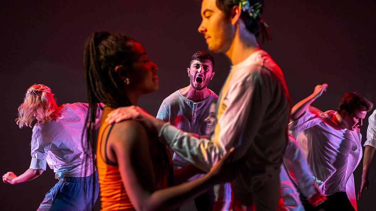 Two actors out of focus in the foreground in loving embrace with jealous actor peering at them