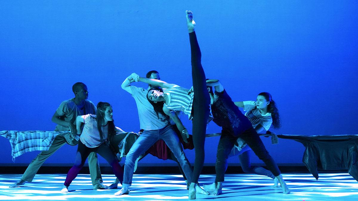 Dancers on stage, main focal being a female dancer with her leg completely vertical