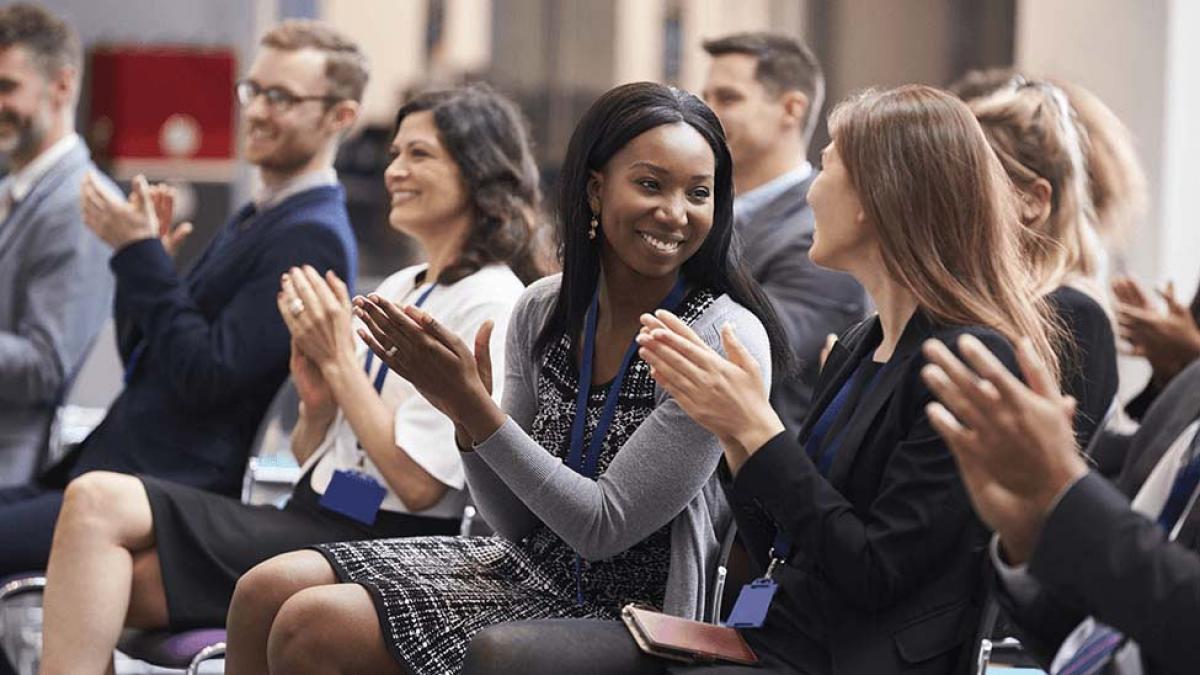 a woman smiles at her colleague as they applaud at a conference