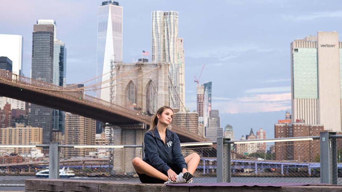 A woman performs a butterfly yoga pose in front of the New York skyline.