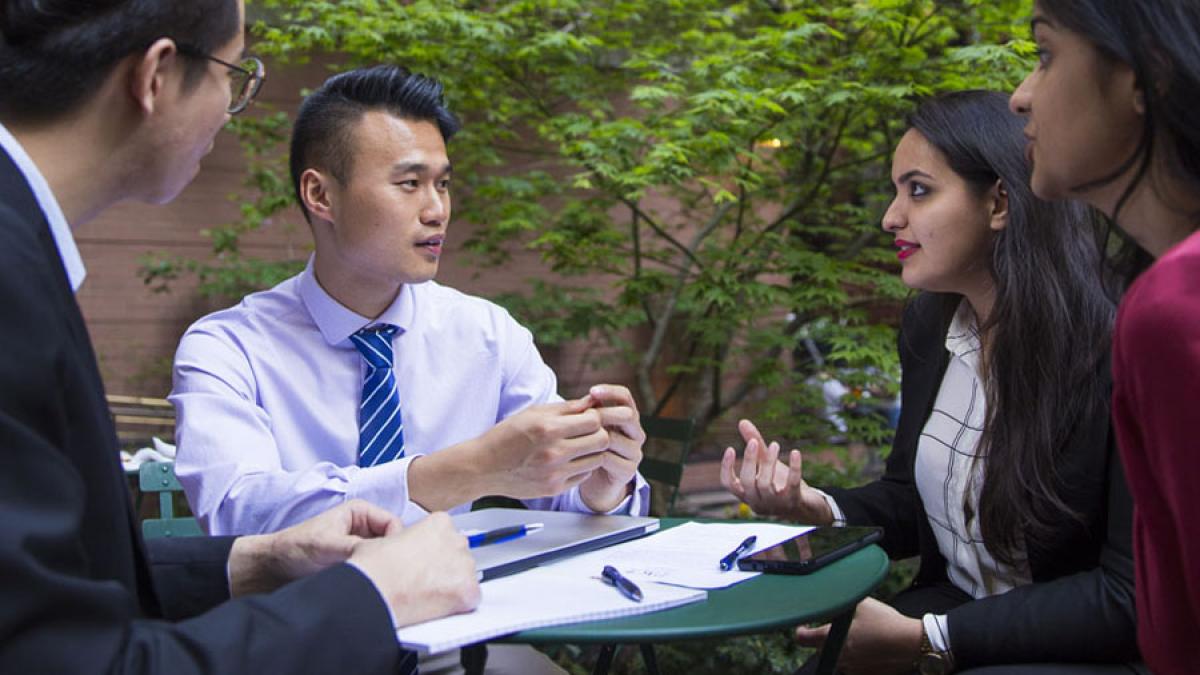 four Lubin graduate students in business attire sitting at a table in Lower Manhattan near Pace University's New York City Campus