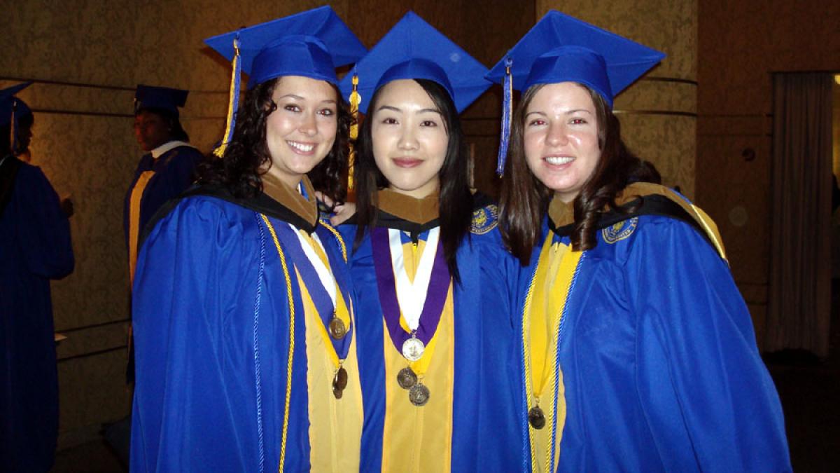 three Lubin alumnae wearing honor cords, caps, and gowns at graduation ceremony