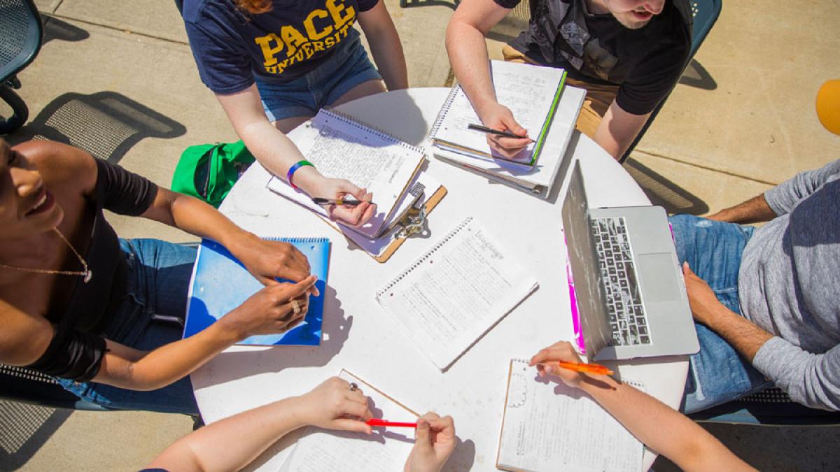 Pace students sitting at an outdoor table with notebooks and laptops on the Pleasantville Campus